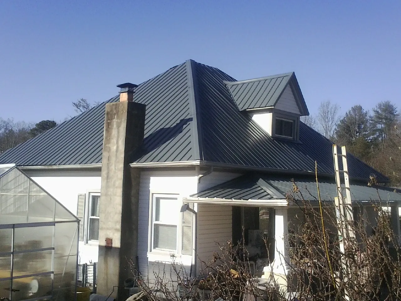 Dark blue standing seam metal roof on a white farmhouse with dormer — Slate & Tile Roof Repair by Roofing Brothers in Wynnewood