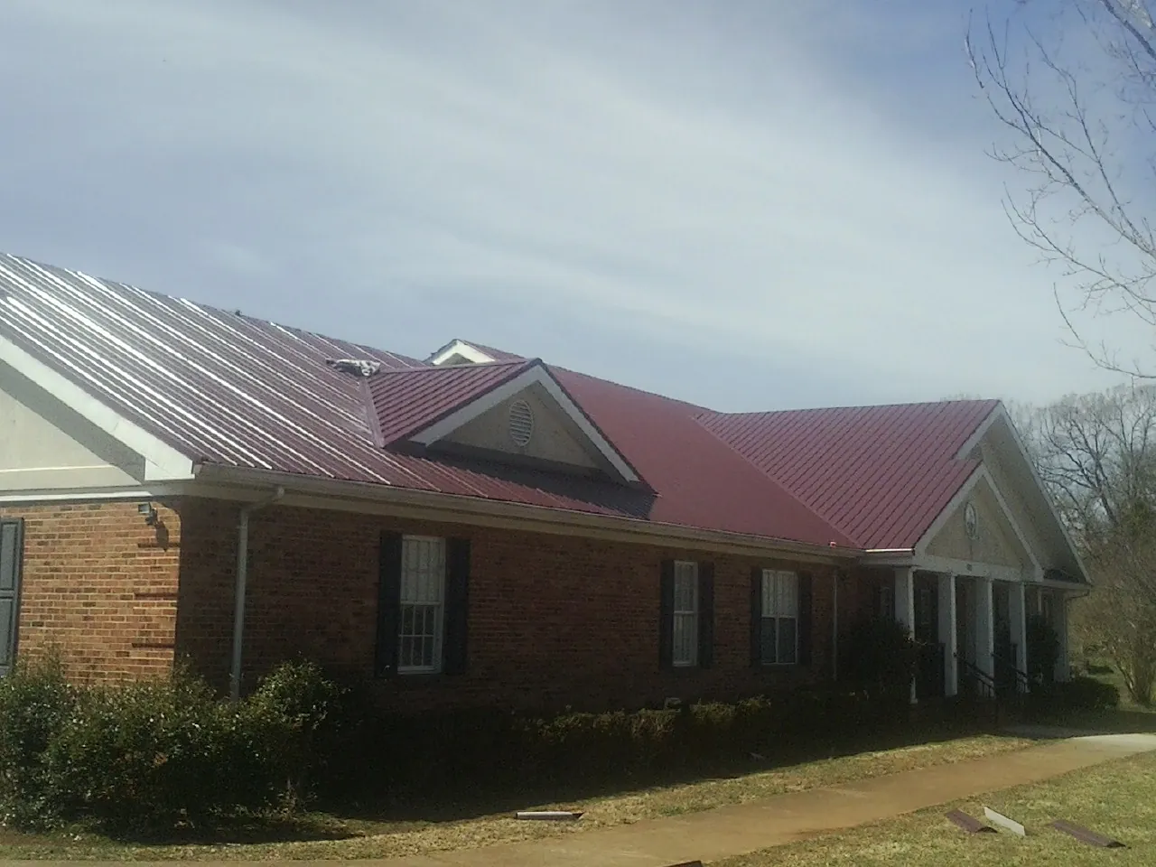 Red metal roof with gabled entries on a long brick building, from a Hail Damage Roof Repair job in Wynnewood