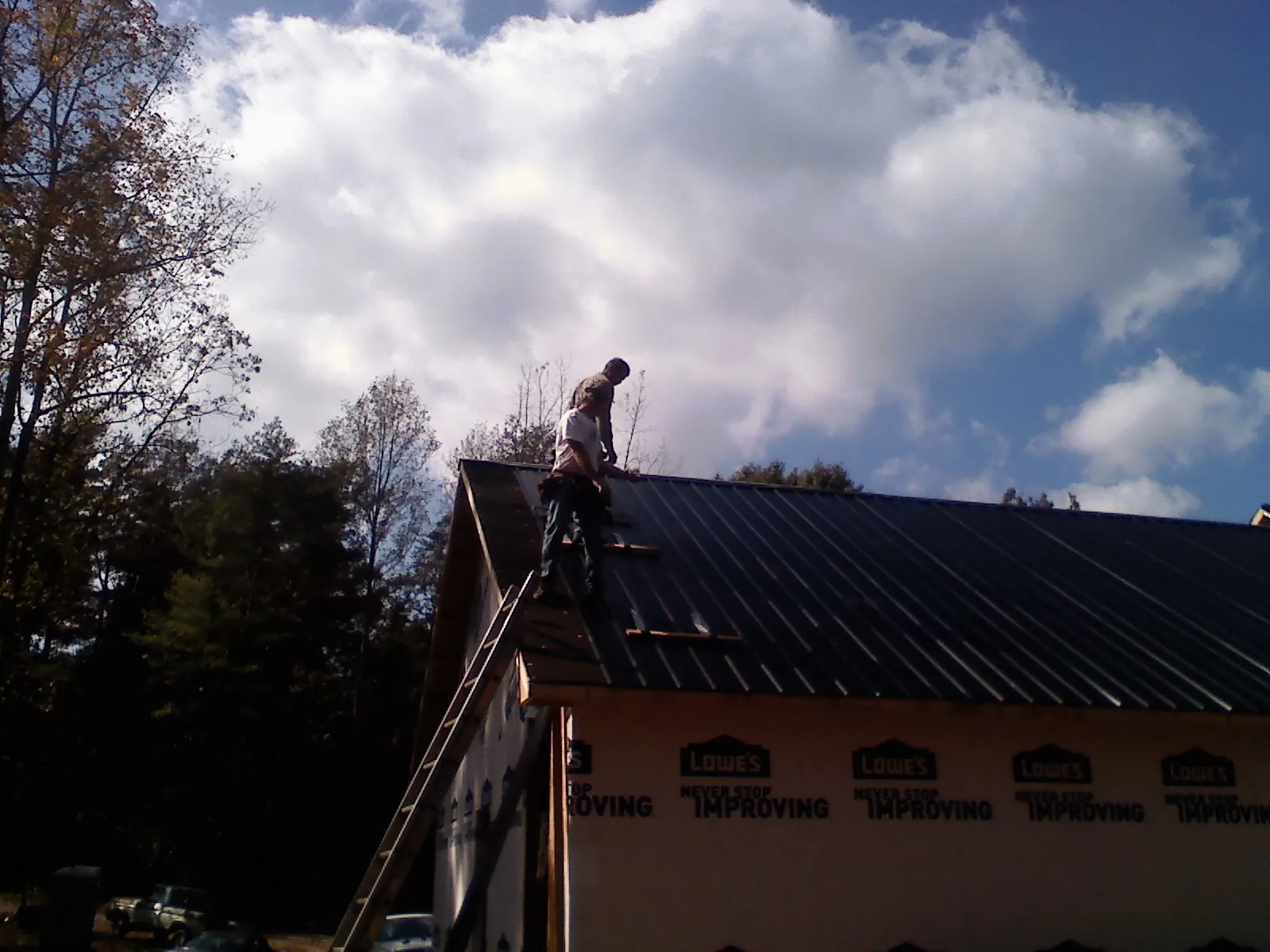 Roofer fastening dark metal panels high against a cloudy sky, from a Roof Inspection job in Wynnewood